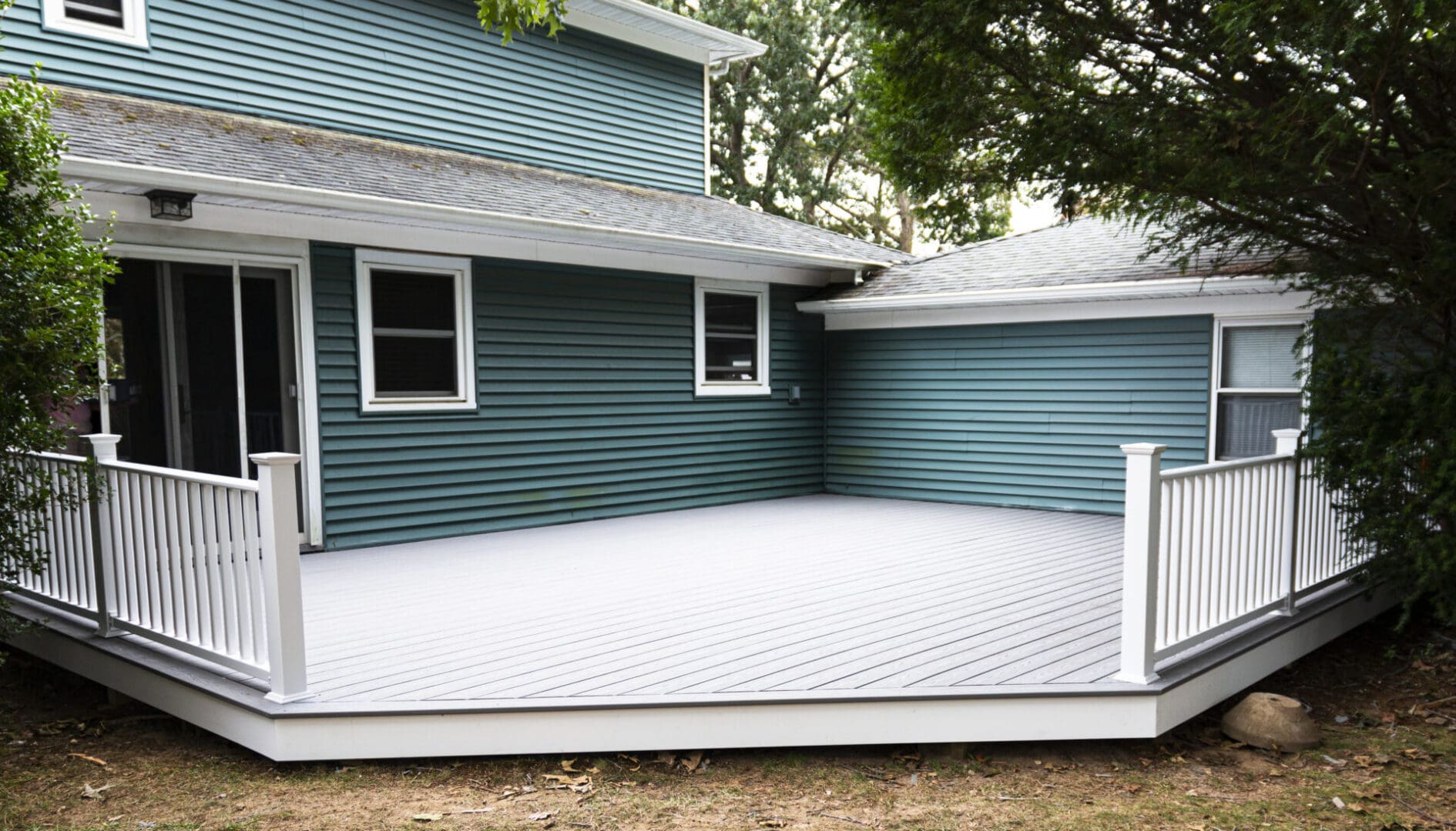 A new deck is installed on the back of a house with composite material and white hand rails.